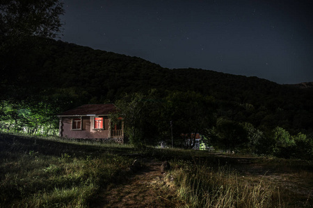 晚上在森林里建筑的山夜风景与月亮或老式乡下房子在晚上与云彩和星.