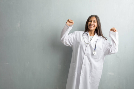 年轻的印度医生对墙上的女人非常高兴和兴奋, 举起双臂, 庆祝胜利或成功, 赢得彩票