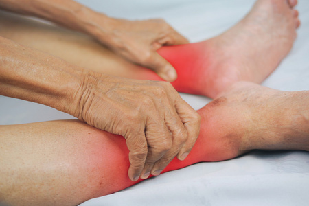 足区老人手里拿着他健康的脚和按摩脚踝疼痛区照片