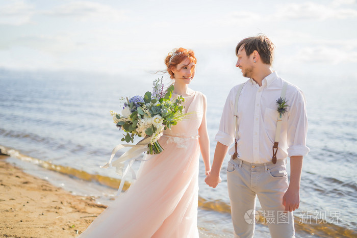 对幸福的夫妻新郎和新娘的婚礼花束是在沙滩上