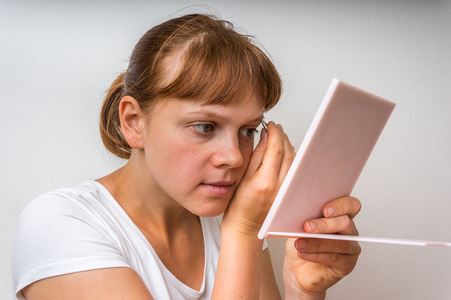 女人用镊子在镜子前拔眉毛