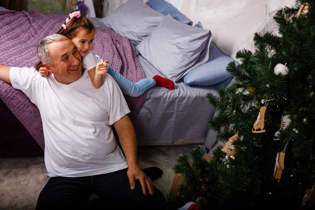 快乐的祖父正在给孩子们礼物。他坐在圣诞树旁的沙发上, 面带微笑。