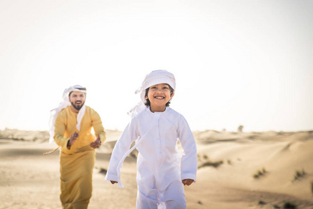 快乐的家庭玩在迪拜的沙漠嬉戏的父亲和他的儿子在户外乐趣