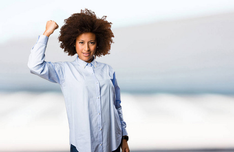 年轻的黑色的妇女在蓝色衬衫做强烈的手势在模糊的背景