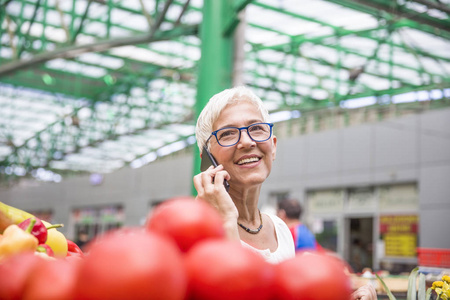 老年妇女在市场上购买蔬菜和使用手机的肖像