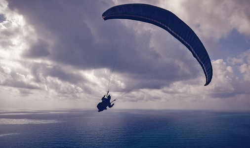 一个人的剪影飞行在滑翔伞高在海之上在云彩, 体育, 秀丽和自由概念