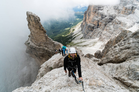 一群年轻的登山者在陡峭的通过 Ferrata 与意大利白云岩的宏伟的看法在他们后面巴迪亚