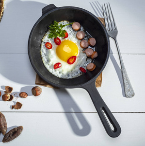 黑圆煎锅配炸鸡蛋和香肠在白色桌上, 顶部查看, 早餐