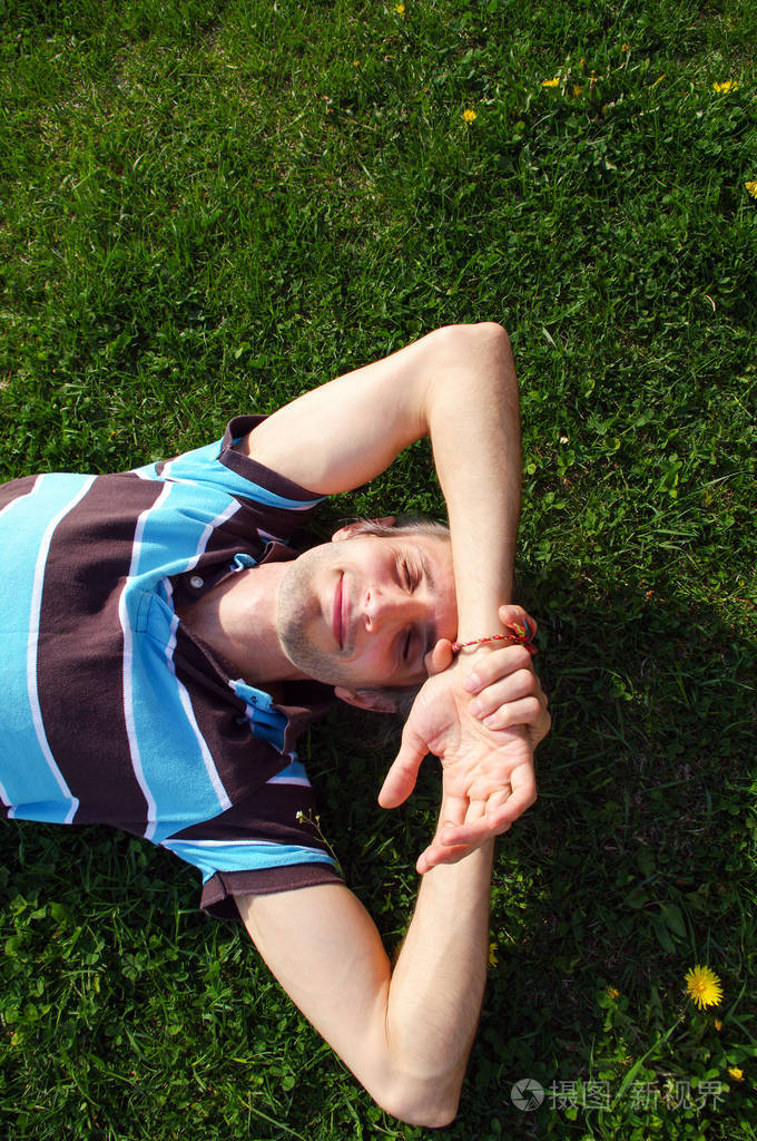 一个年轻人快乐轻松的用手在头下的草地上的肖像