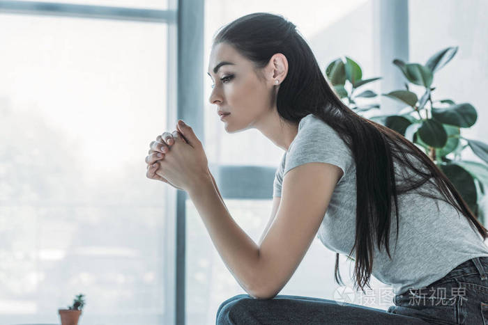 坐在家里的伤心的黑发女人的侧面视图