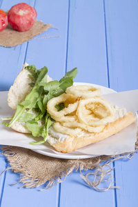 美味的油炸戒指三明治, 配有白色圆板, 半面包, 洋葱和绿色芝麻菜沙拉