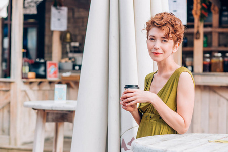 一个美丽的女人在夏日咖啡馆里, 手里拿着咖啡, 微笑着看着相机。