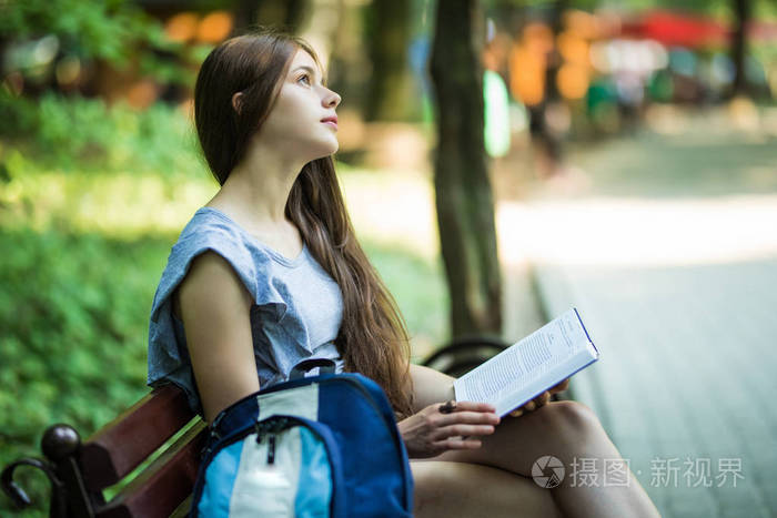 快乐的黑发女郎，坐在公园长椅上的手里拿着笔记本