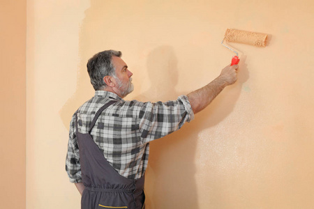 在房间里画墙的工人用漆辊涂上橙色的颜色