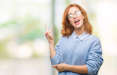 年轻美丽的女人在与世隔绝的背景下穿着冬衣微笑着, 脸上带着快乐的面孔眨着眼睛做着胜利的手势。第二个