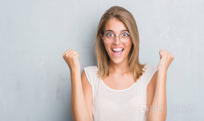 美丽的年轻女子站在灰墙上戴着眼镜, 尖叫着自豪和