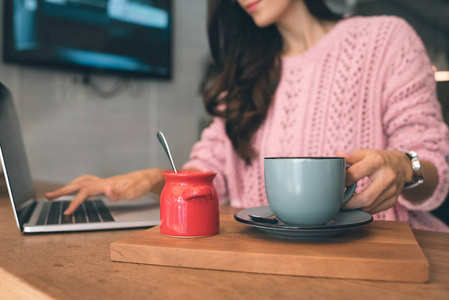 女性自由职业者的裁剪图像坐在笔记本电脑和咖啡杯在咖啡馆的桌子上