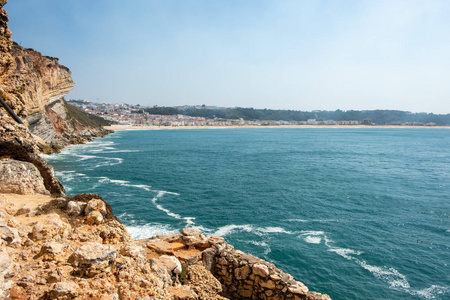 Nazare, 葡萄牙2018年9月20日 金黄石头峭壁绿色海并且 Nazare 的村庄在背景 Nazare, 葡萄牙