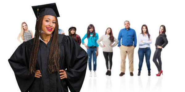 年轻毕业的黑人妇女戴辫子与手在臀部, 站立, 放松和微笑, 非常积极和开朗
