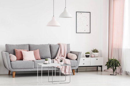 粉红色枕头在灰色沙发在白色公寓内部与海报和灯以上表。真实照片