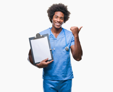 美国黑人外科医生拿着剪贴板人在孤立的背景指向和显示与拇指到一边, 快乐的脸微笑着