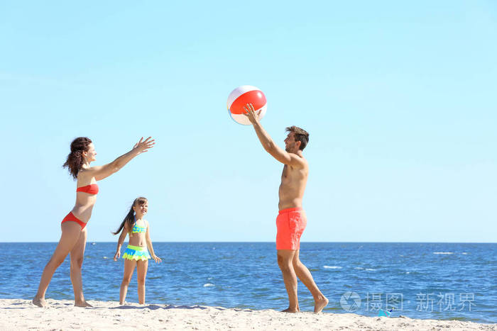 家庭观念。父母和女儿在沙滩上玩球