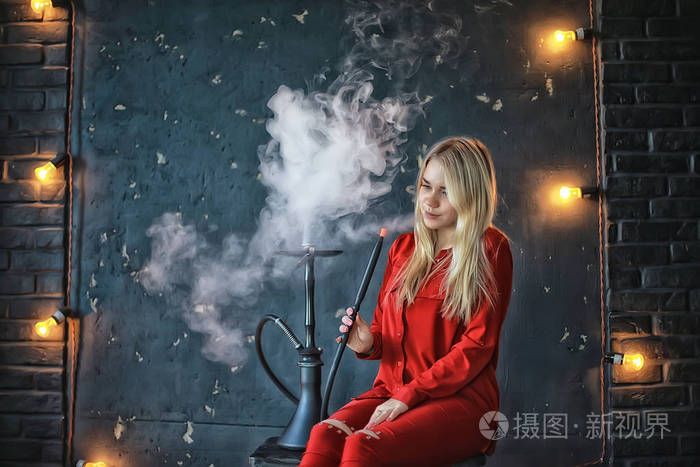 有吸引力的年轻金发女子在红色衣服吸烟水烟