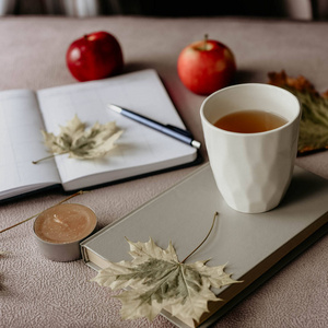 杯茶与书在里面与秋天叶子, 笔记和红色苹果 hygge 概念照片