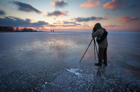 摄影师在冬天冰冻的河上拍摄日落的图片