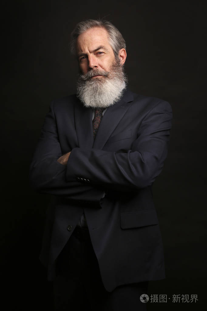 深色头发和满胡子的老人, 穿着西装在黑暗背景下关闭