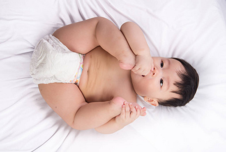 肖像的可爱的小亚洲男孩 6 个月大把他脚趾的脚在嘴里白色的床上，
