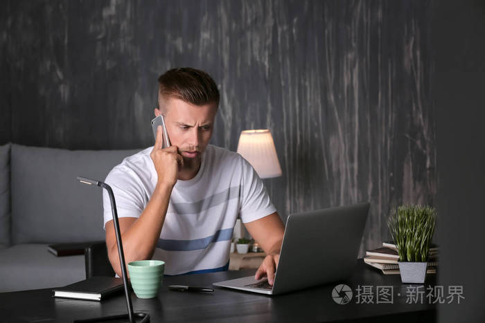 年轻的自由职业者的电话交谈, 而在笔记本电脑晚上工作