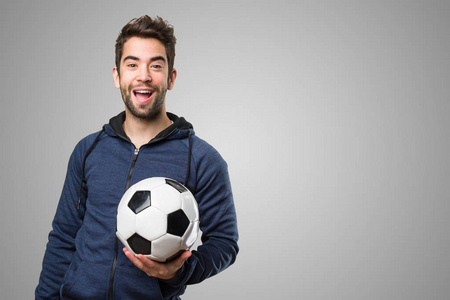 在灰色背景举行足球的快乐的年轻人