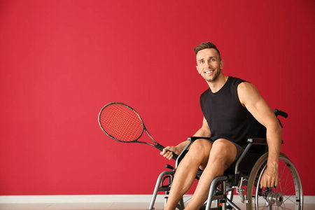 年轻的网球选手坐在轮椅上反对彩色墙