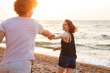可爱的年轻幸福的情侣的形象漫步在海滩上互相牵手