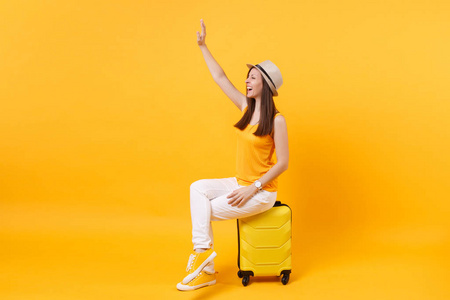 旅游者在夏季休闲服装, 帽子坐在手提箱上, 黄色橙色背景。在周末外出旅行的女乘客。航空飞行旅途概念