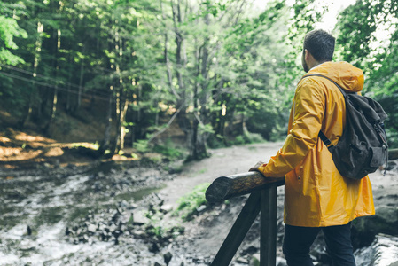 男子站在森林中间的黄色雨衣。徒步旅行概念