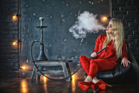 有吸引力的年轻金发女子在红色衣服吸烟水烟