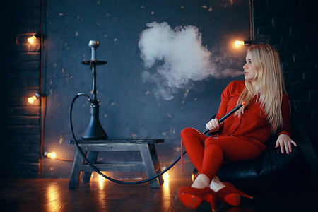 有吸引力的年轻金发女子在红色衣服吸烟水烟照片