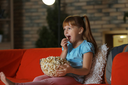 晚上在沙发上看电视的小女孩吃爆米花