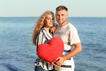 可爱的年轻夫妇持有红色的心在海岸边