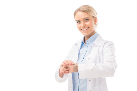 微笑的年轻女医生检查时间腕表, 看着相机在白色隔离