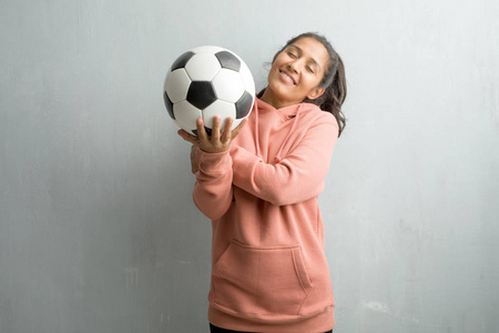 年轻运动的印第安妇女反对墙壁骄傲和自信, 指向手指, 例子跟随, 满意的概念, 傲慢和健康。拿着足球玩游戏