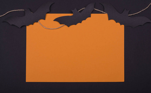 橙色手工方形框架与黑纸蝙蝠, 交在黑色背景上的绳子。平躺
