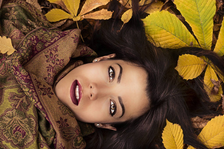 美丽的年轻女子在秋天的一天，躺在地上用色彩鲜艳的秋叶