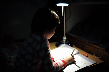 小亚洲女孩的肖像在昏暗的房间照明灯下做作业照片