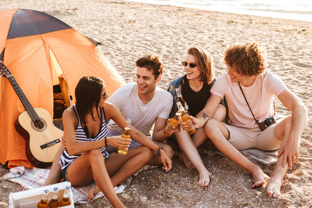 在海滩上的朋友兴奋小组的照片坐在一起喝啤酒聊天