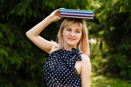 开朗的年轻学生女孩抱着书在她的头上, 微笑着