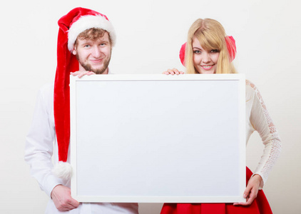 几个女人和男人抱着空空白横幅与副本空间。在圣诞老人的帽子和英俊的男人，在灰色的工作室的漂亮女孩。圣诞节圣诞节广告