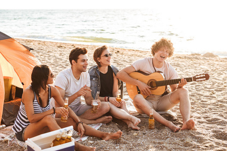 一群兴奋的年轻朋友一起在海滩玩, 喝啤酒, 玩吉他, 而露营